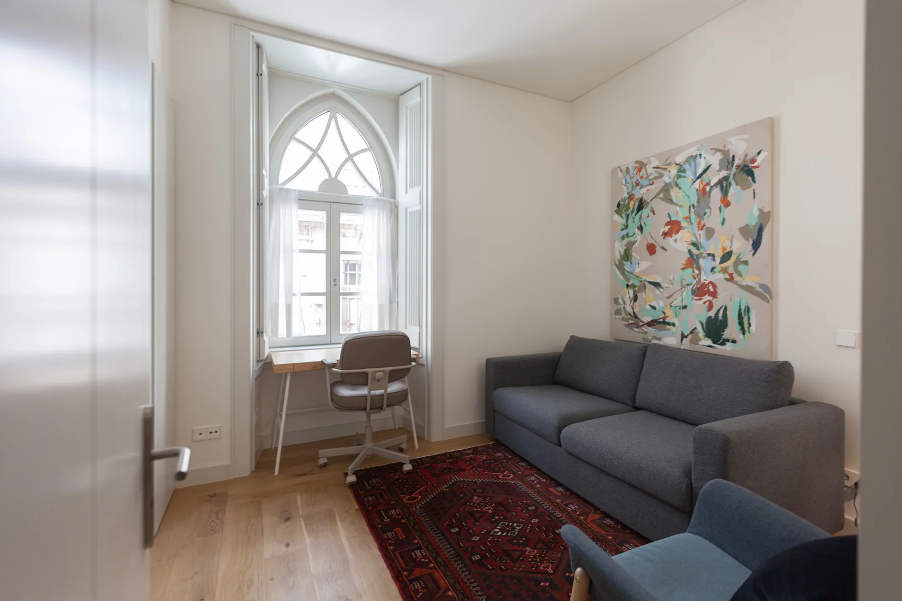 A living room with seating, a desk, and colorful artwork on the wall.