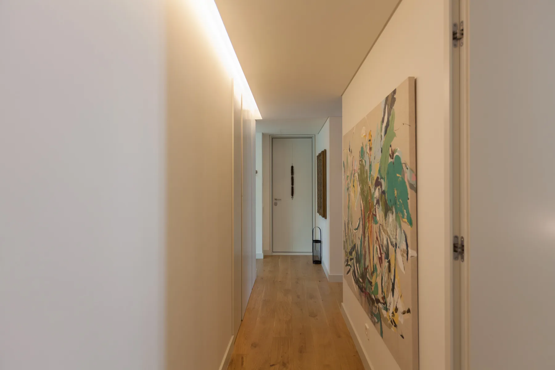 A hallway with wood flooring and colorful artwork on the wall.