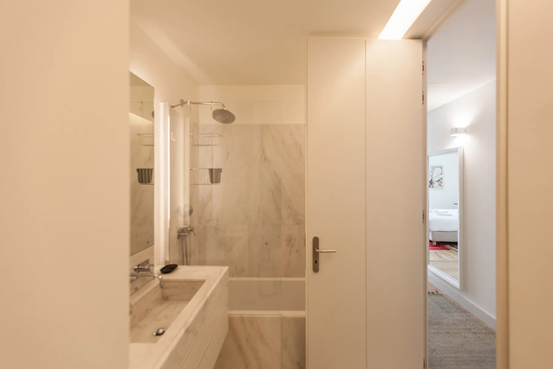 A bathroom with a sink and shower, viewed through an open doorway.