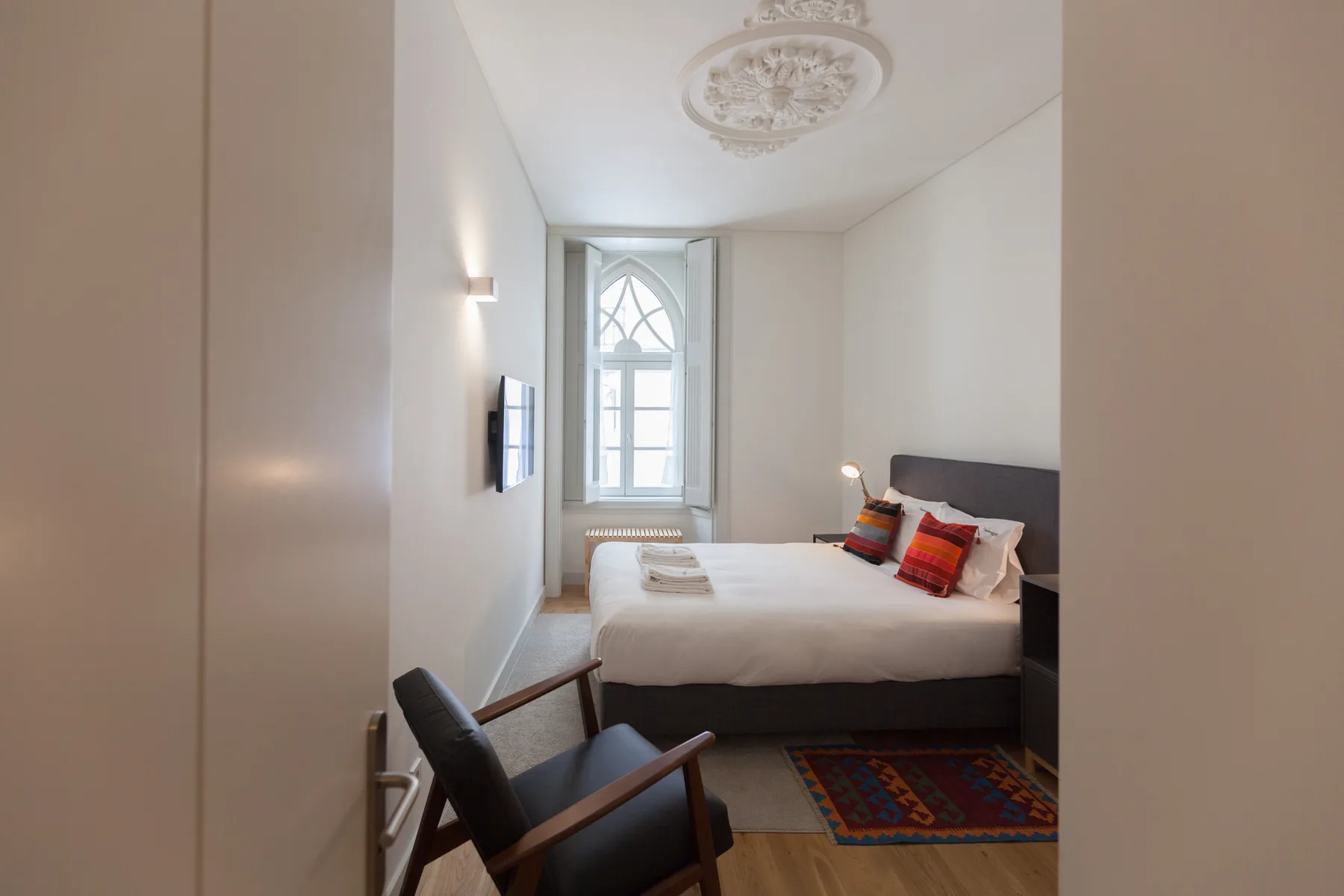 A bedroom with a bed, an armchair, and a tall window.