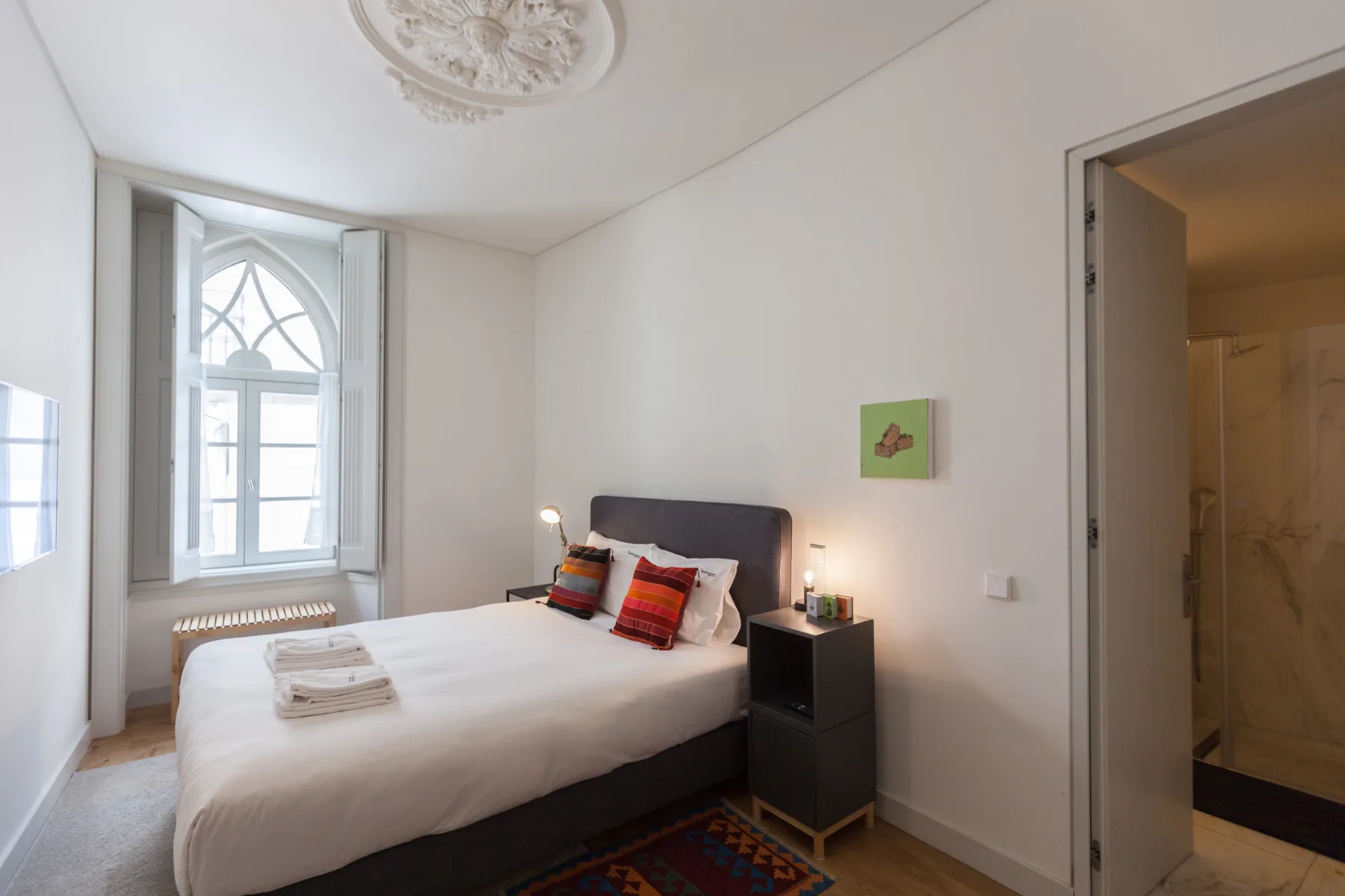 A bedroom with a bed beside a tall arched window.