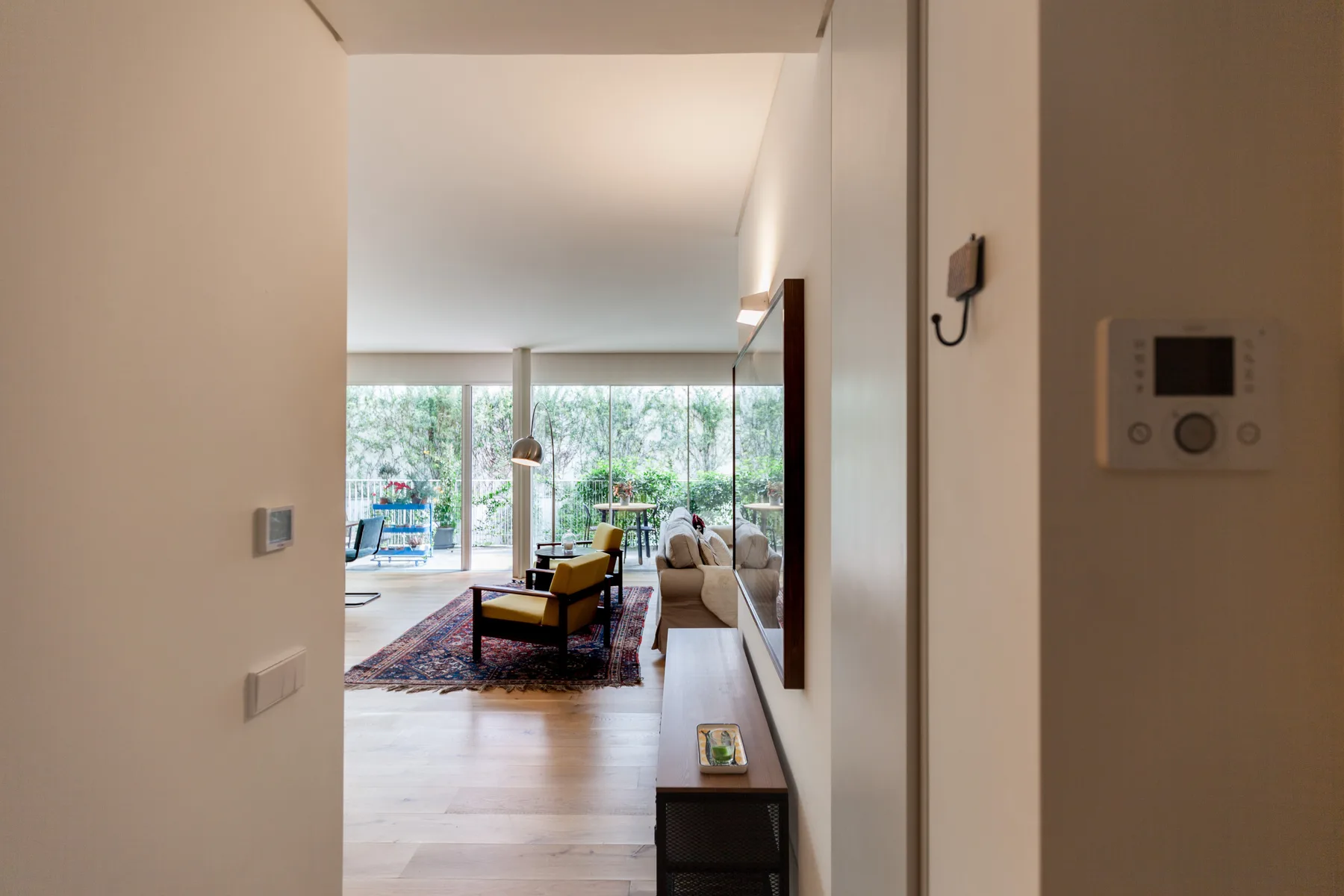 A bright living room with seating and large windows overlooking greenery.