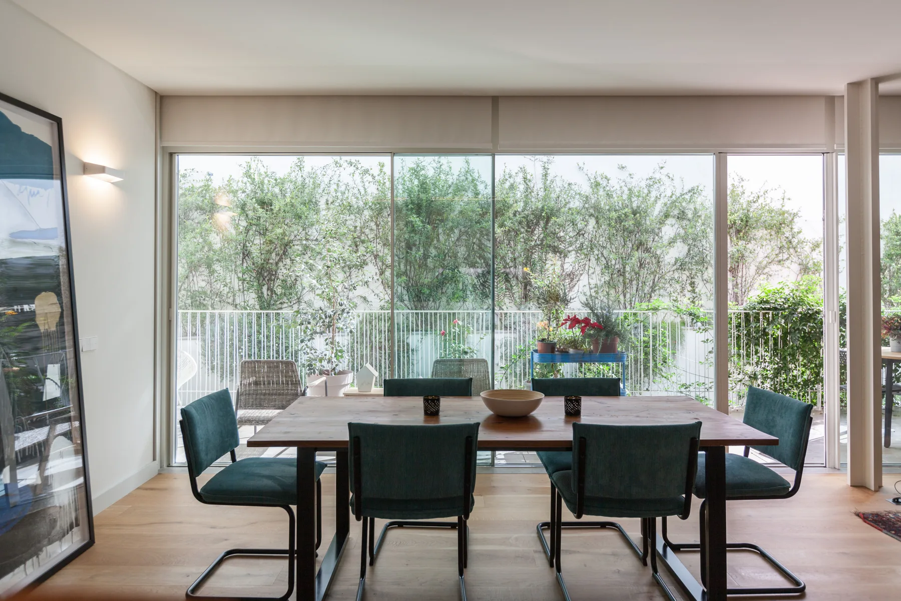 A dining area with a table and seating beside large windows overlooking greenery.
