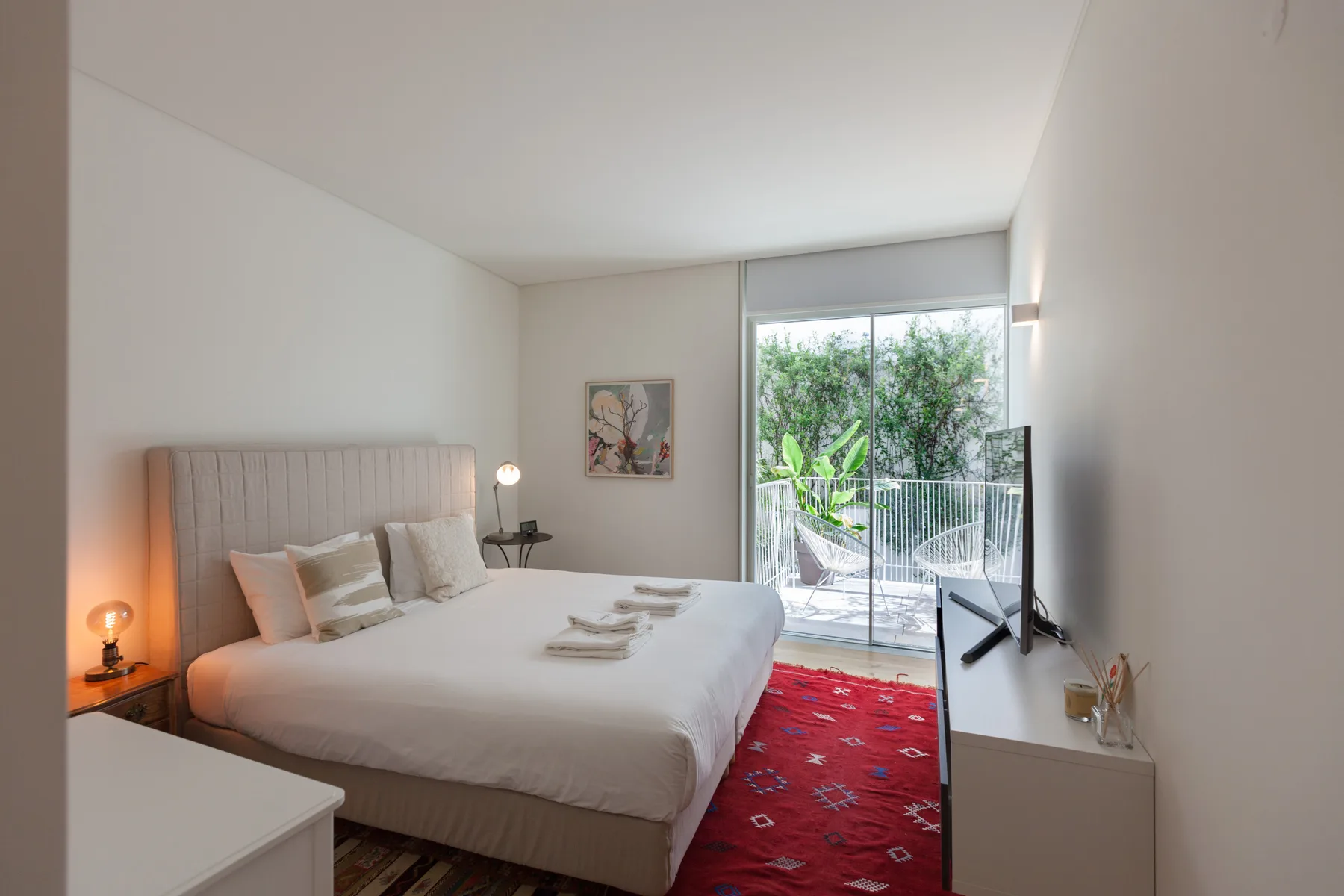 A bright bedroom with a neatly made bed and sliding glass doors opening to a balcony.