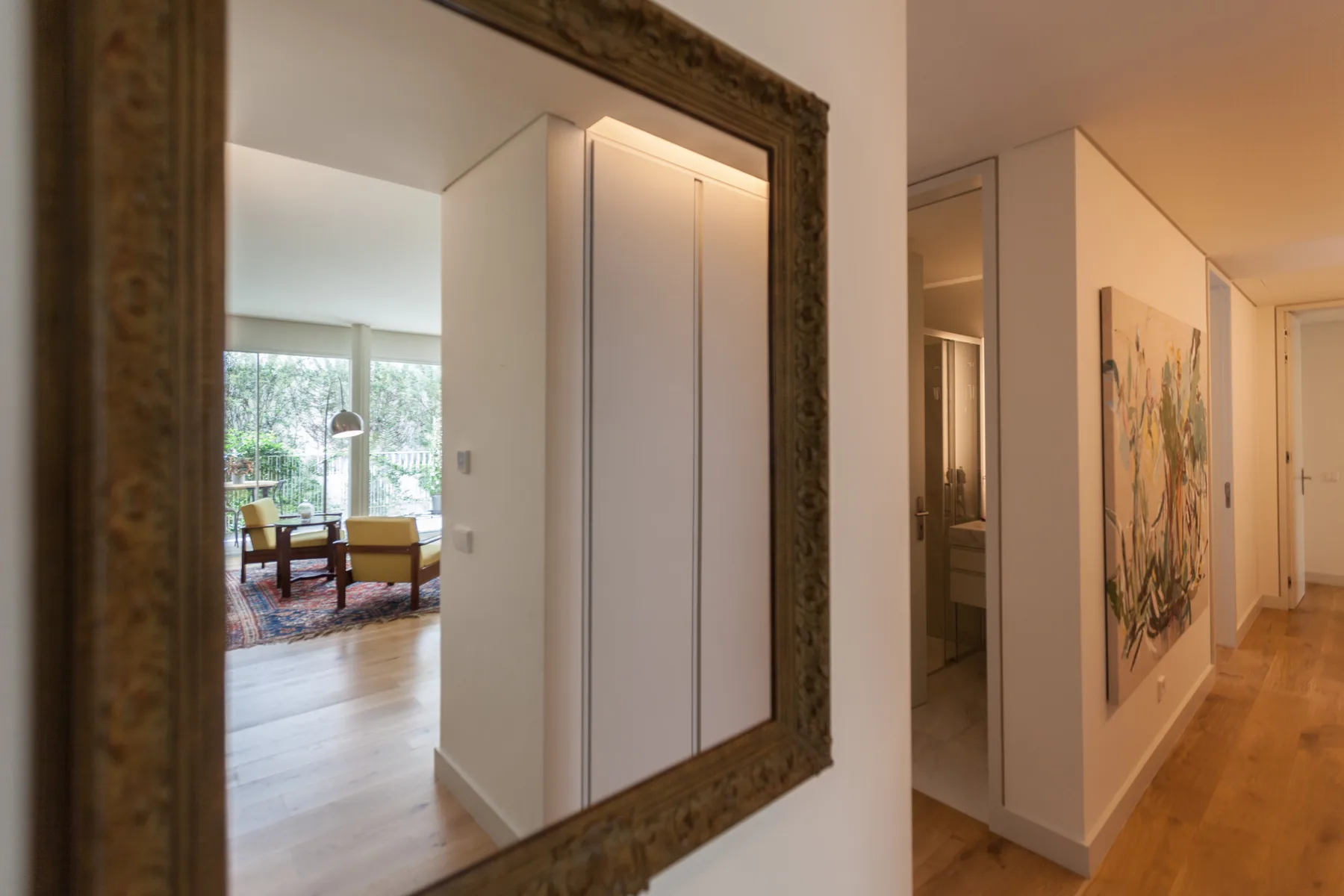 A hallway with a large wall mirror and a view into a furnished living area.