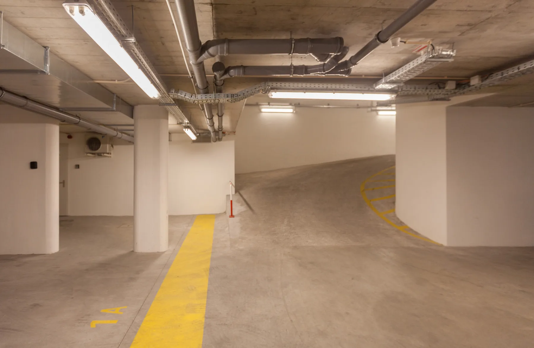 An indoor parking garage with painted yellow lane markings and exposed ceiling pipes.
