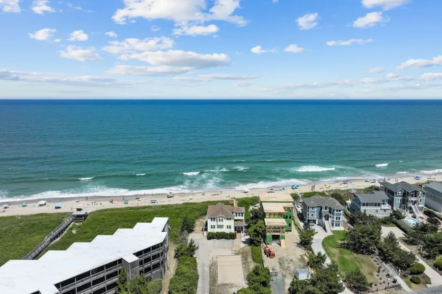 Aerial view of beachfront homes beside the ocean under a partly cloudy sky.