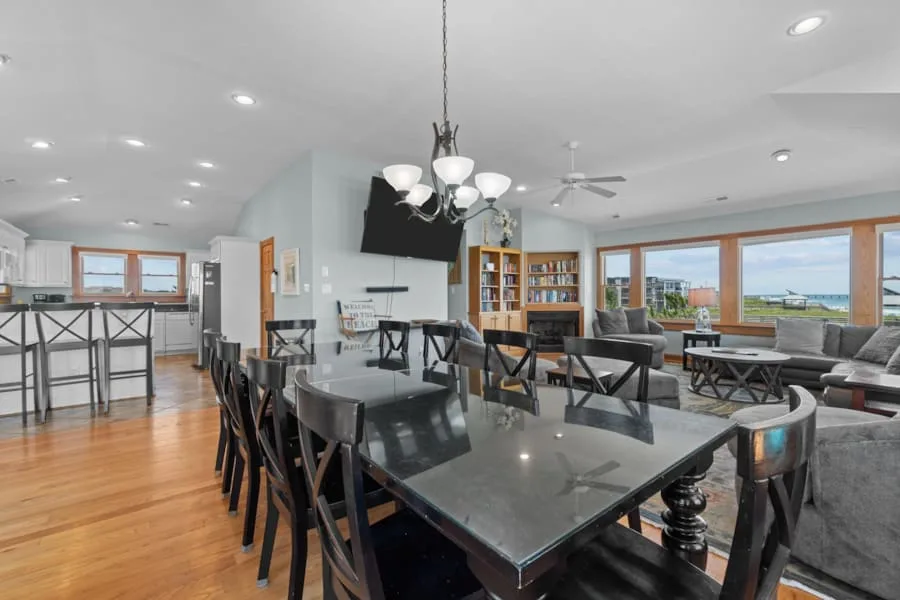 An open-plan dining and living area with a long dining table and large windows.