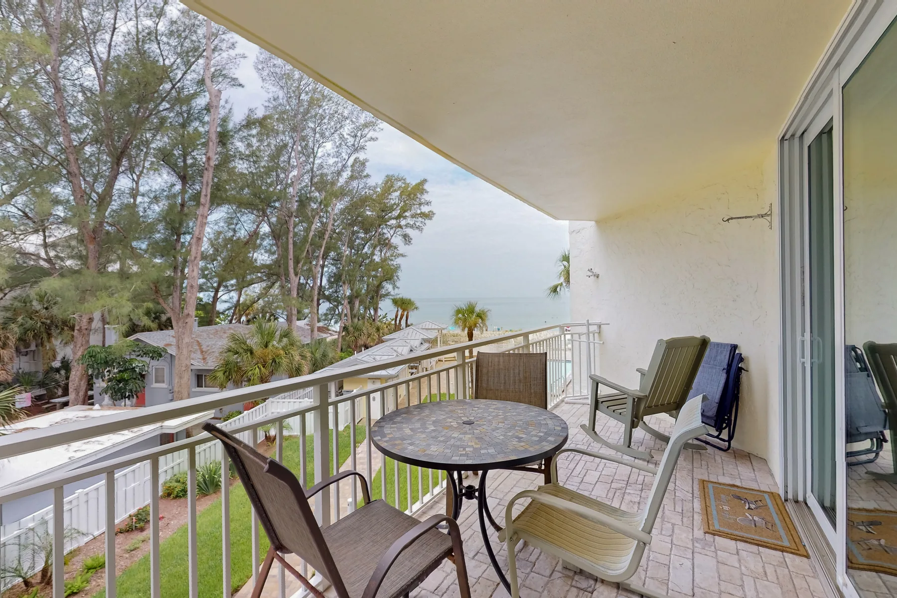 A covered balcony has outdoor seating and a round table overlooking trees and the water.