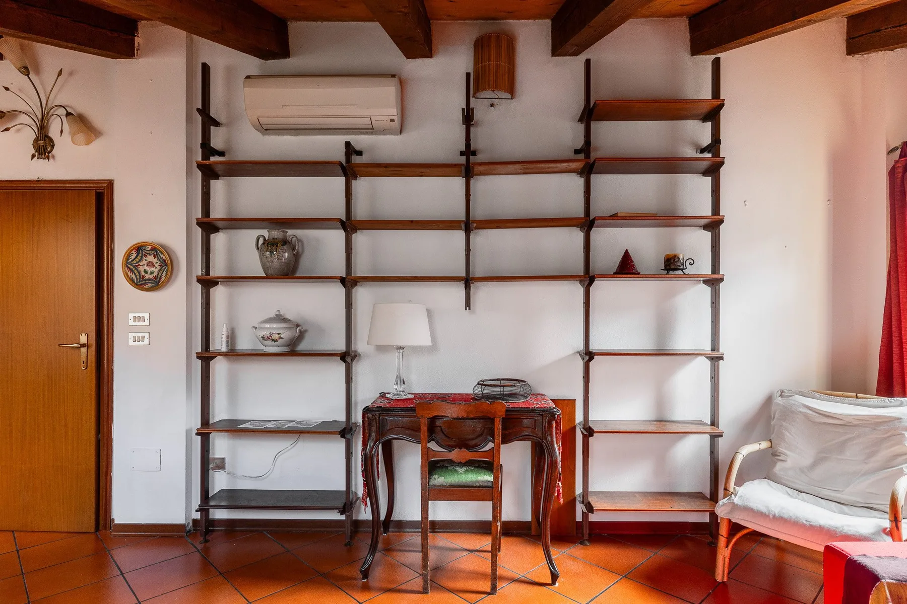 Una habitación con estanterías abiertas y una mesa pequeña bajo vigas de madera vistas.
