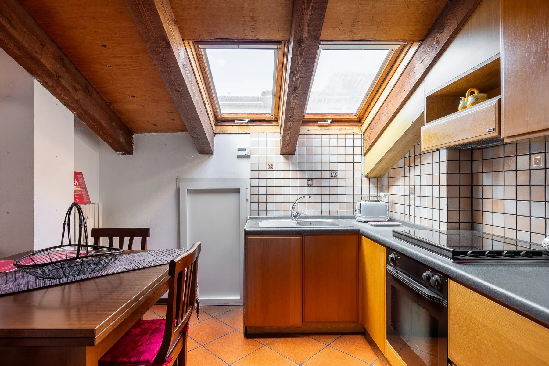 Una cocina compacta con armarios de madera, paredes de azulejos y tragaluces.