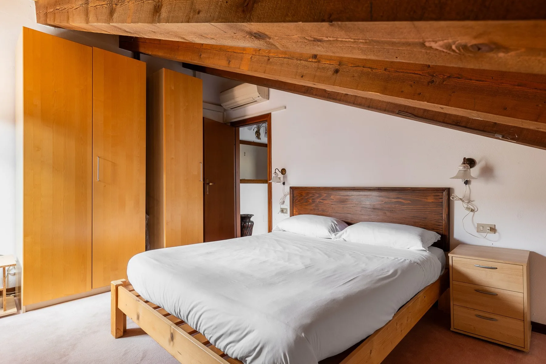 Un dormitorio con una cama doble, armarios de madera y vigas expuestas en el techo.