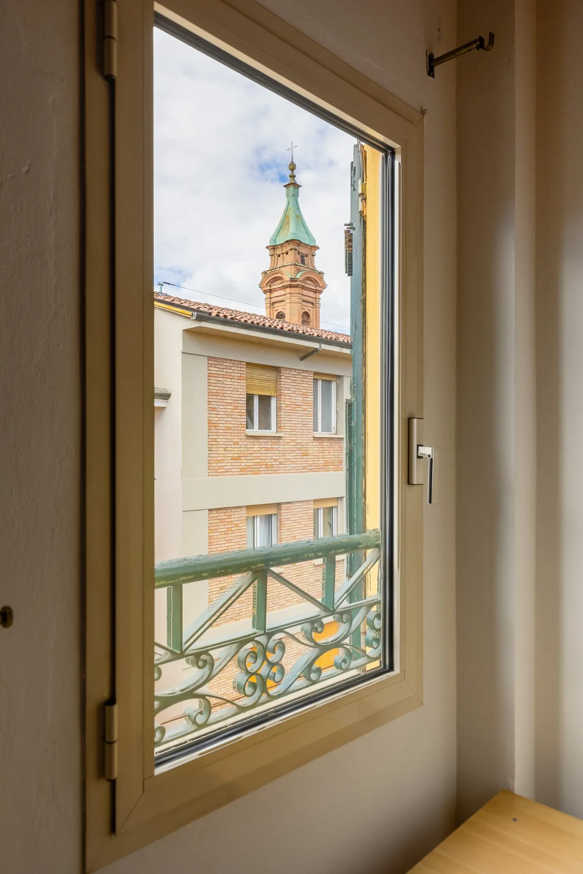 Una ventana de la habitación da a un edificio vecino y una torre de techo verde.