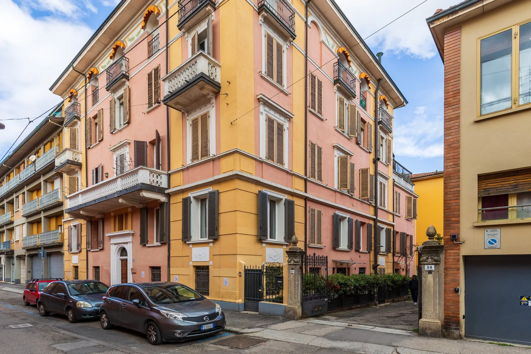 Un edificio rosa y amarillo de varios pisos se encuentra junto a una calle urbana.