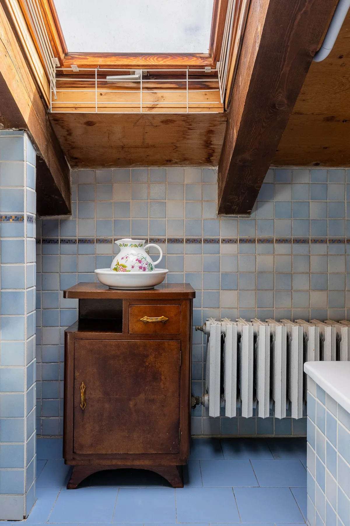 Un baño alicatado con un mueble de madera, un radiador y una claraboya.