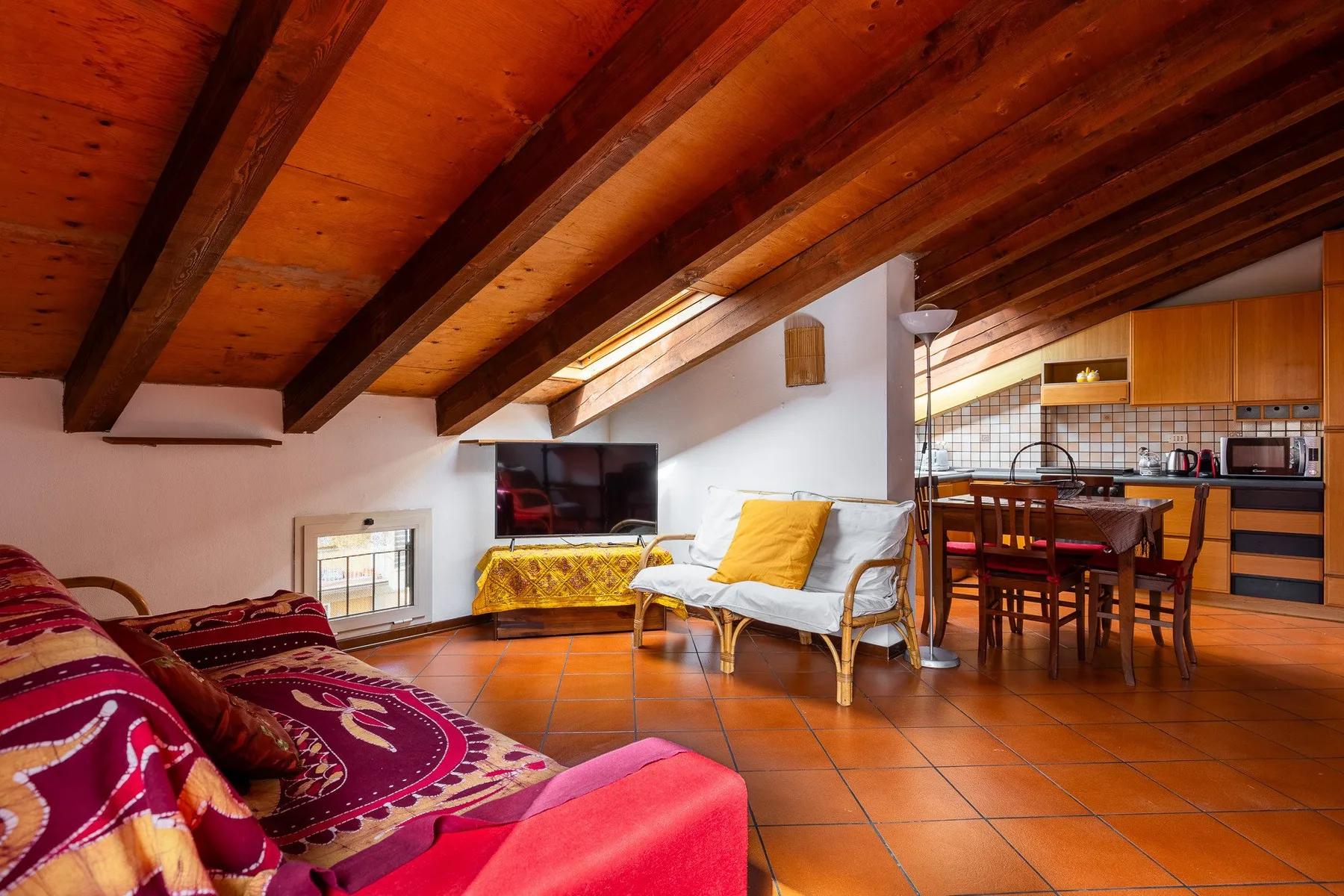 Una acogedora sala de estar con asientos, televisor y mesa de comedor bajo un techo inclinado de madera.
