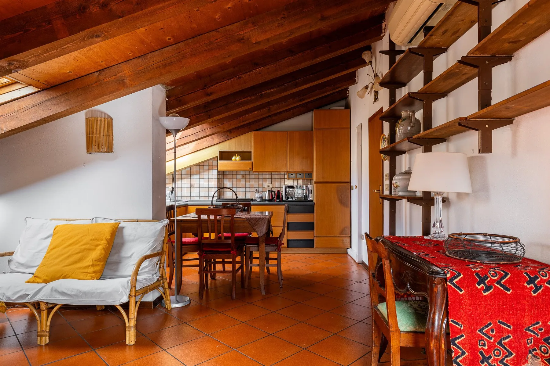 Una sala tipo loft con comedor y cocina compacta bajo un techo inclinado de madera.