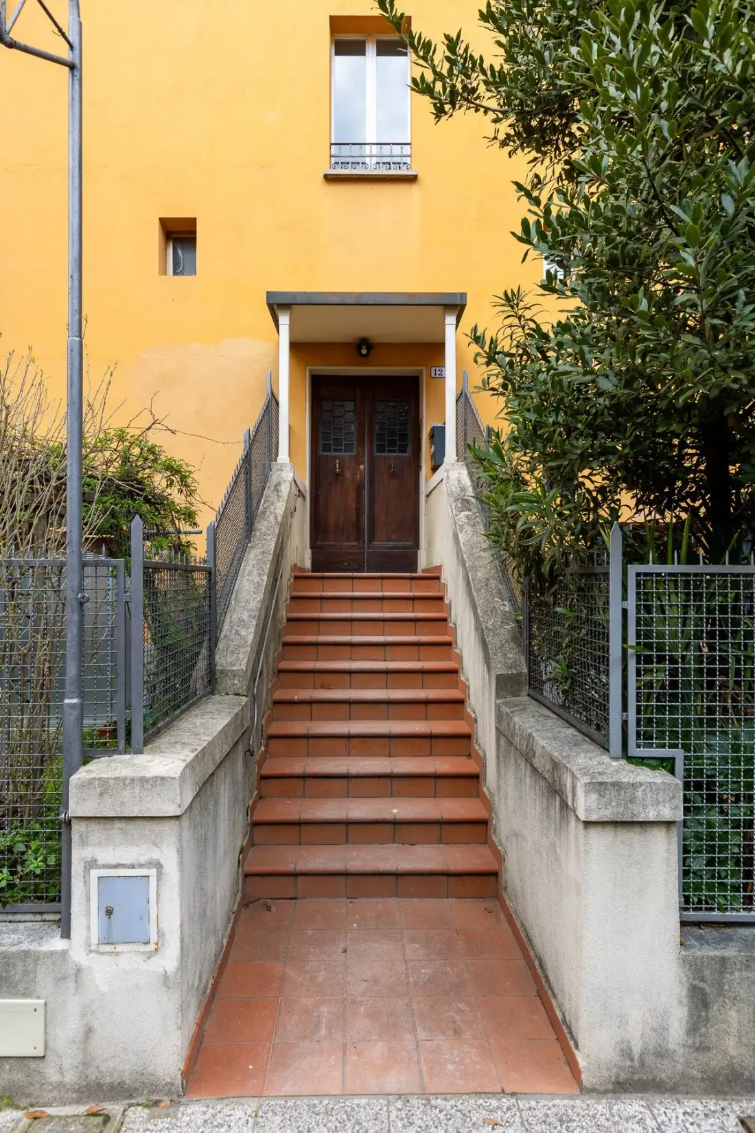 Una entrada exterior con escalones de baldosas conduce a una puerta de madera en un edificio amarillo.