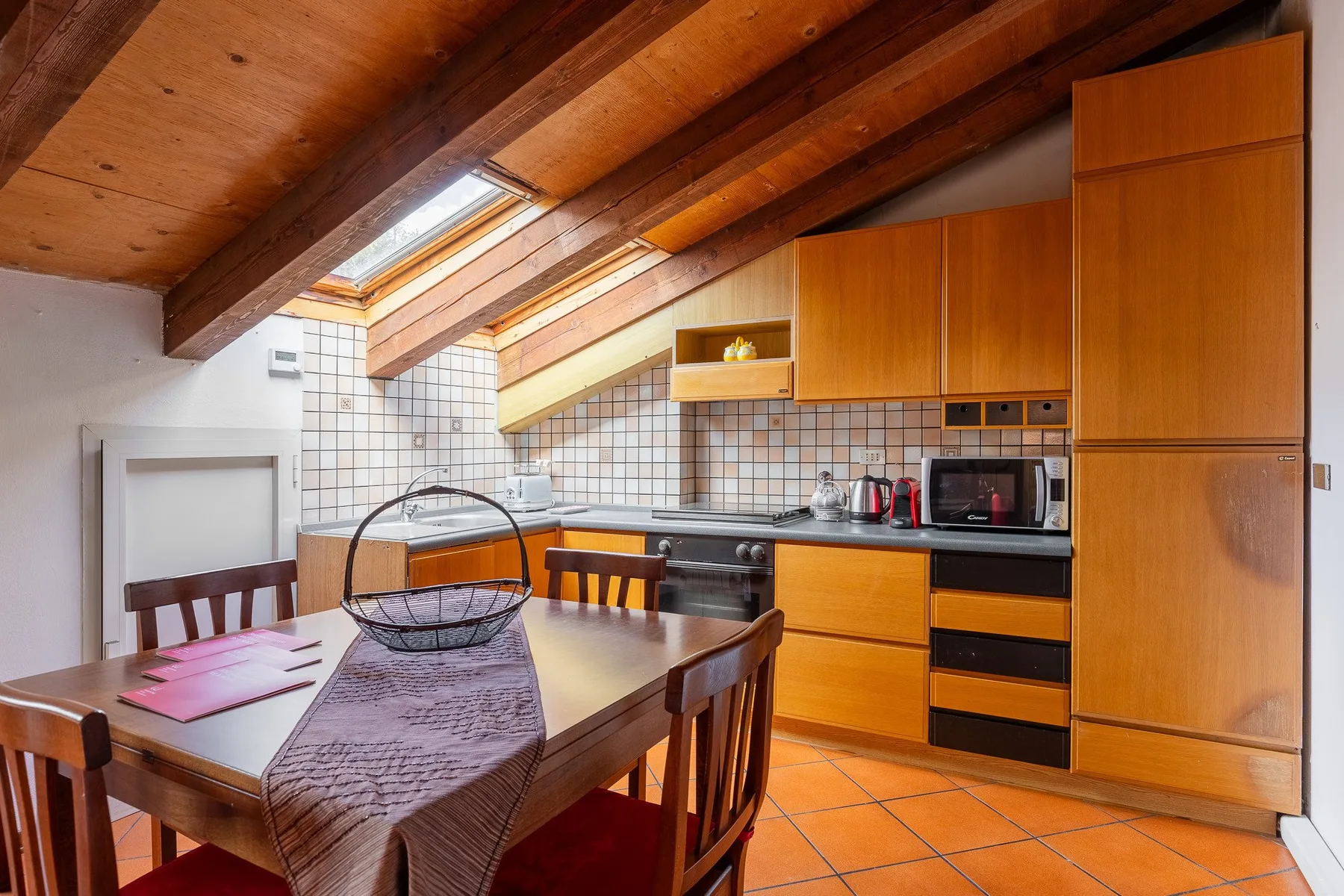 Una cocina y comedor con gabinetes de madera, una mesa y vigas expuestas en el techo.