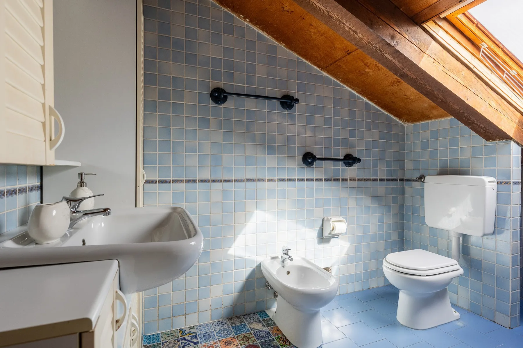 Un baño con azulejos, lavabo, inodoro y techo de madera inclinado.
