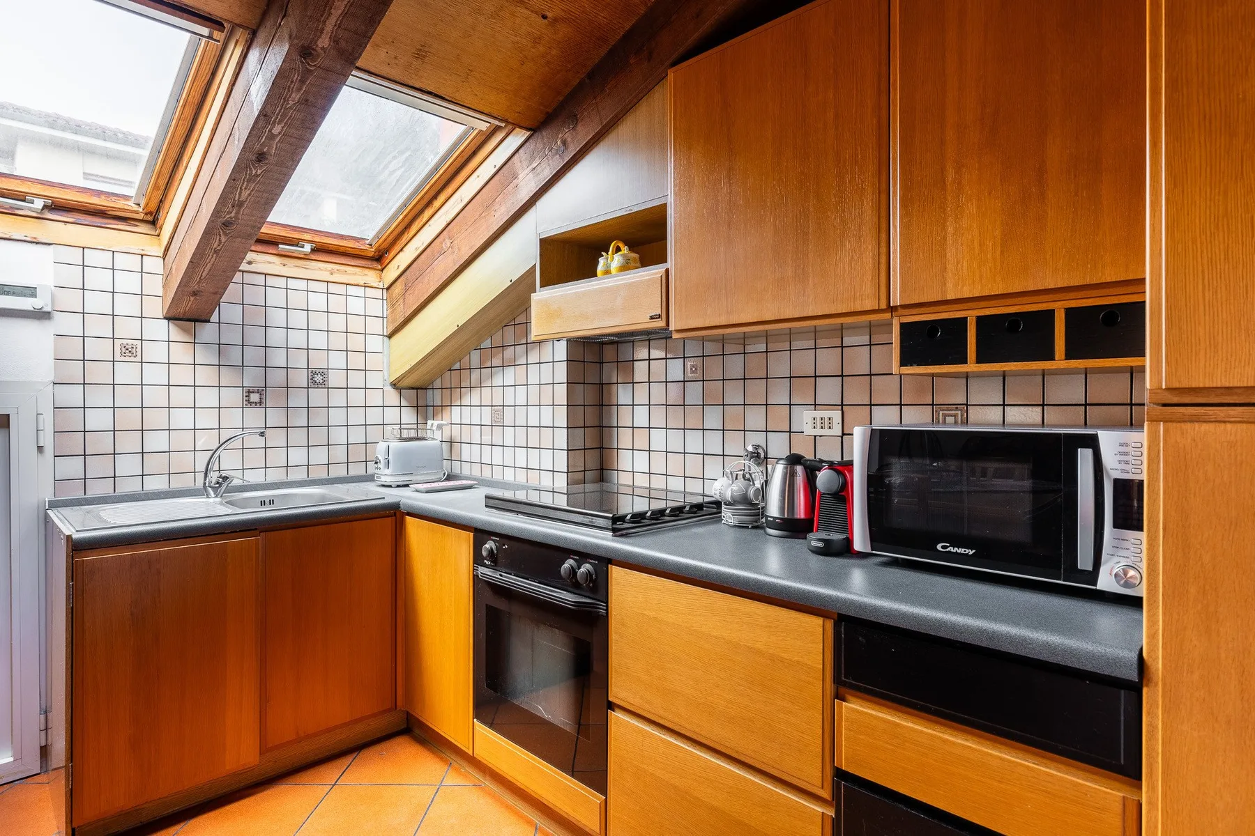 Una cocina con armarios de madera, paredes de azulejos y ventanas en el techo.