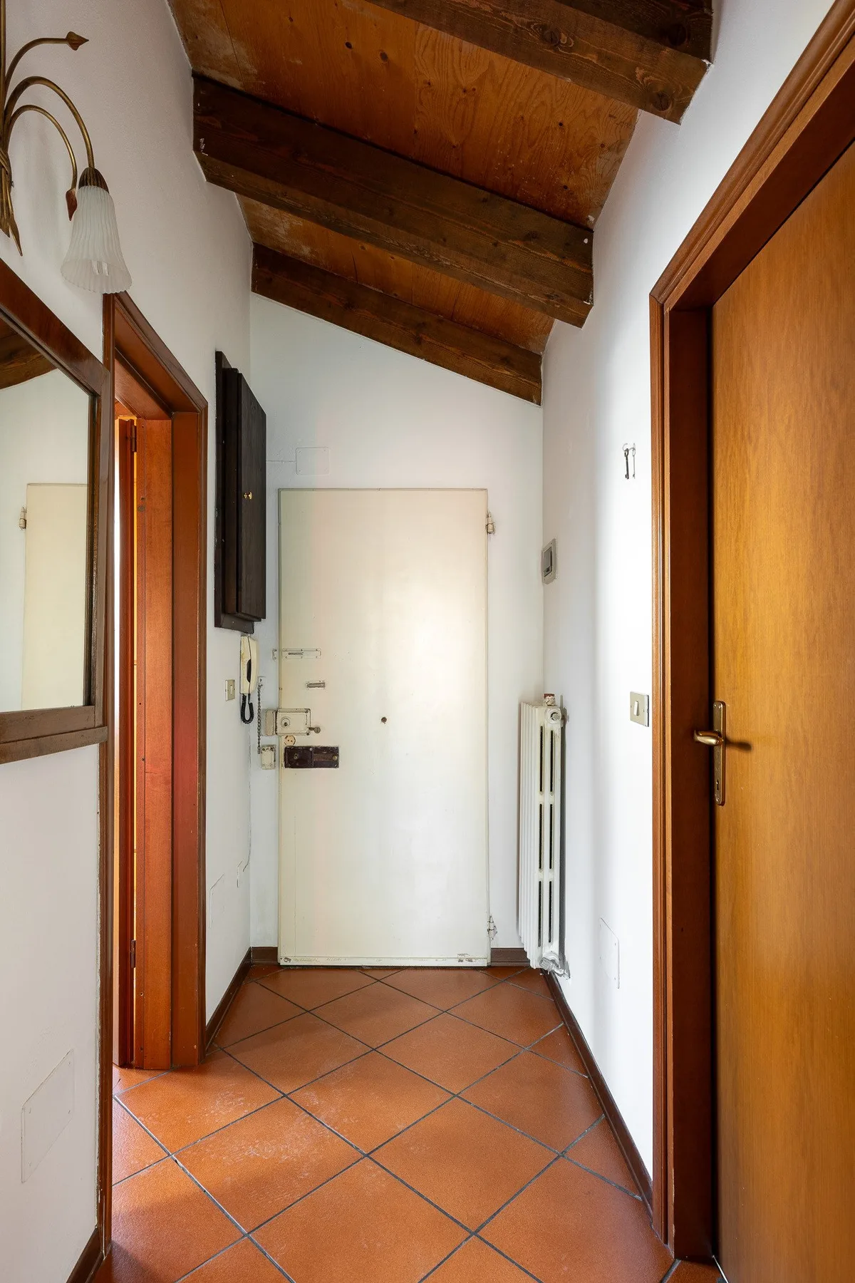 Un pasillo estrecho con suelo de baldosas de terracota, puertas de madera y vigas vistas.