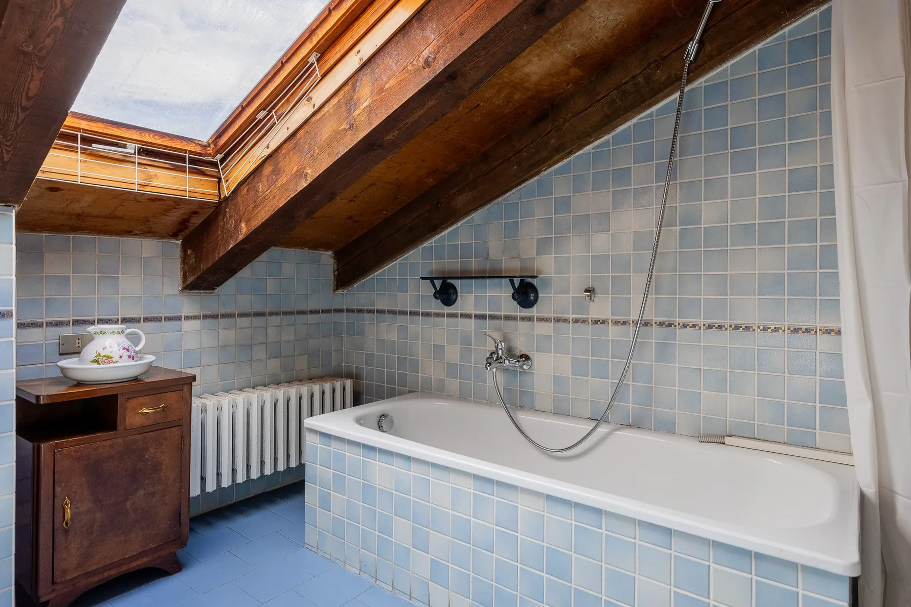 Un baño alicatado con una bañera bajo vigas de madera expuestas.