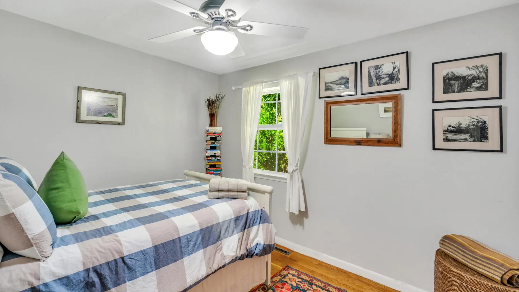 A bedroom with a plaid bedspread, a window, and framed pictures on the wall.