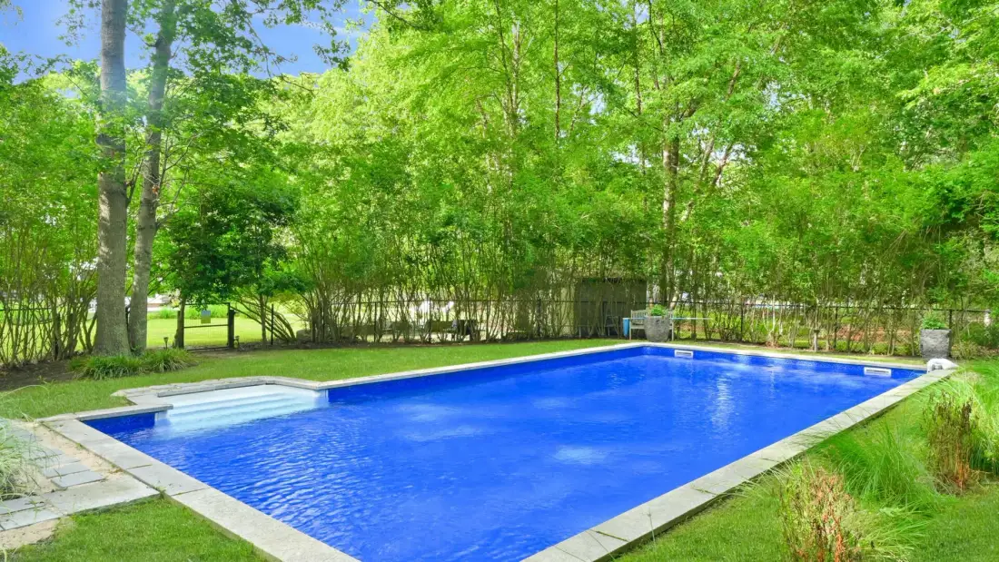 Una piscina azul está junto a un jardín frondoso.