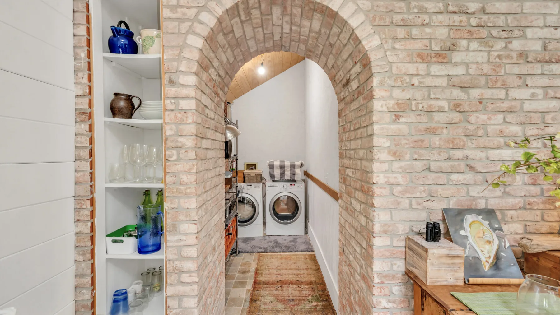 A brick archway opens onto a laundry area with washing machines.