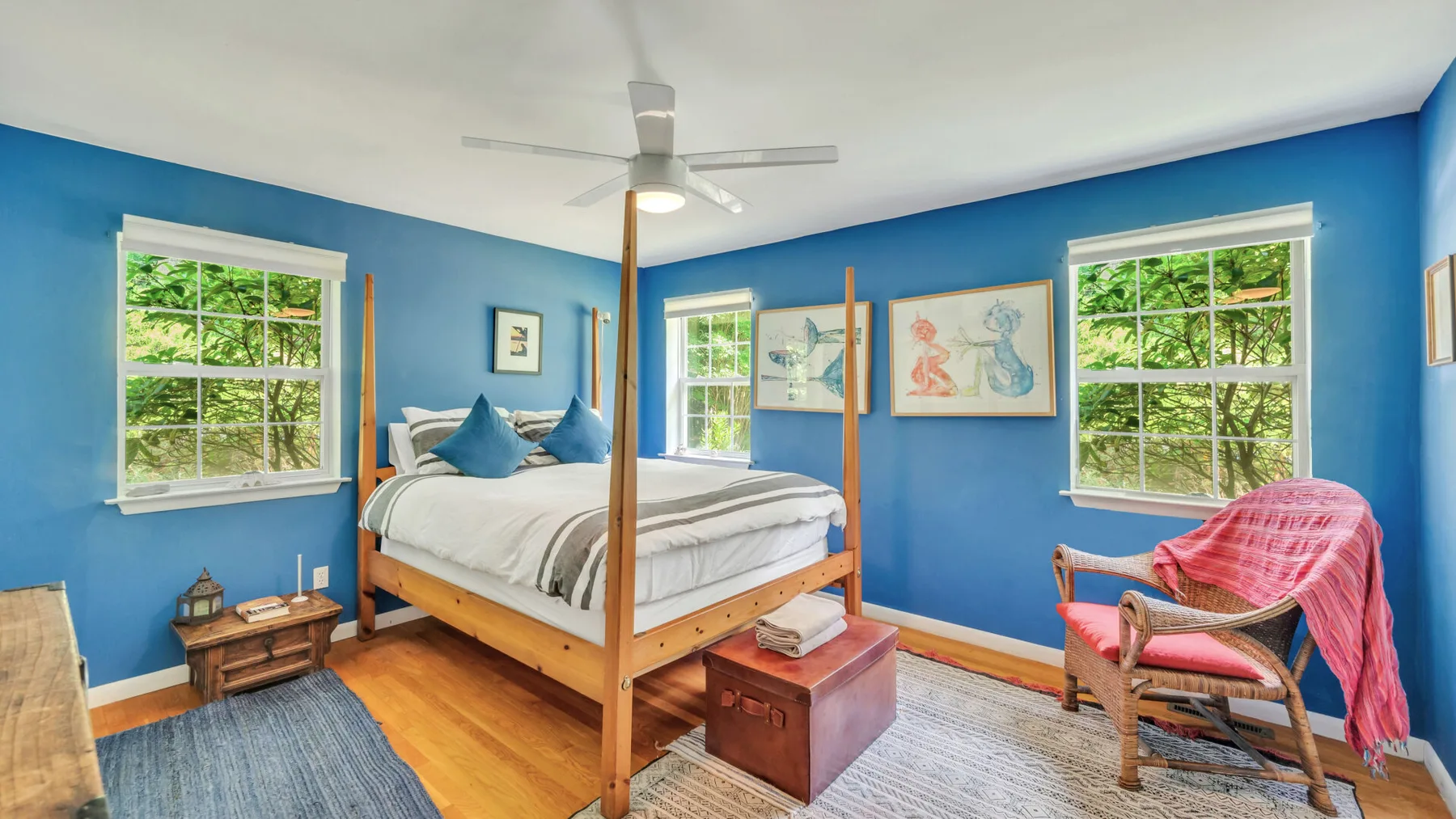 A bedroom with a wooden bed, blue walls, and windows overlooking greenery.