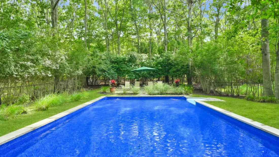 A blue swimming pool surrounded by greenery and trees.