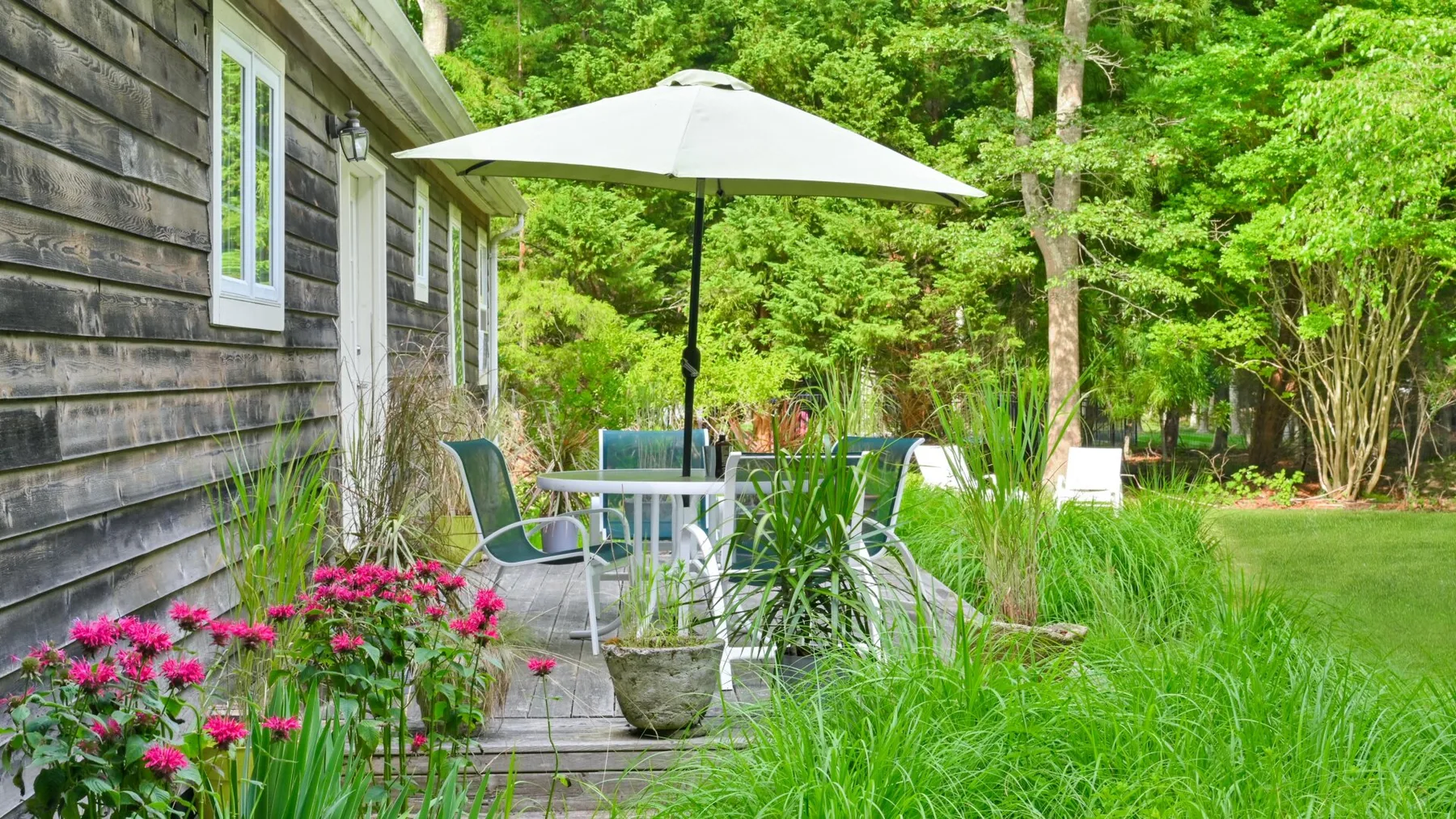 An outdoor patio beside a wooden house has seating under a white umbrella.