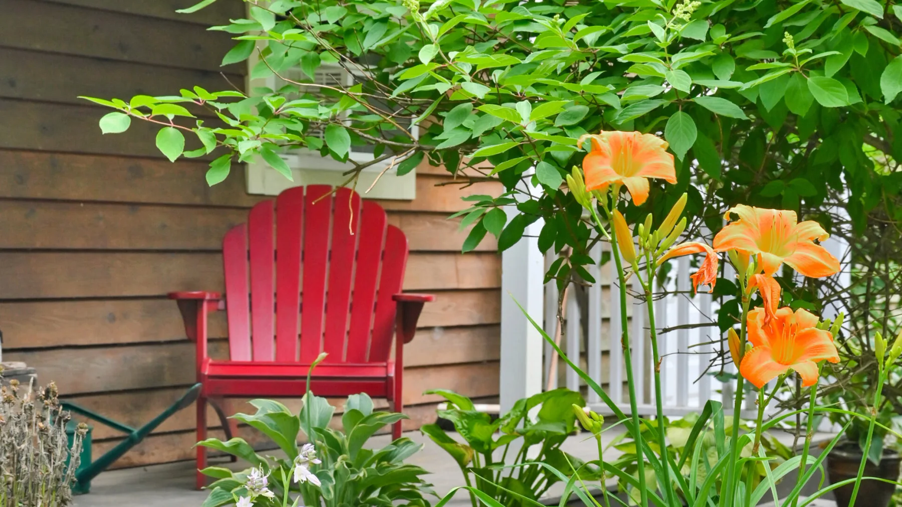 A garden seating area with a red chair beside flowering plants.