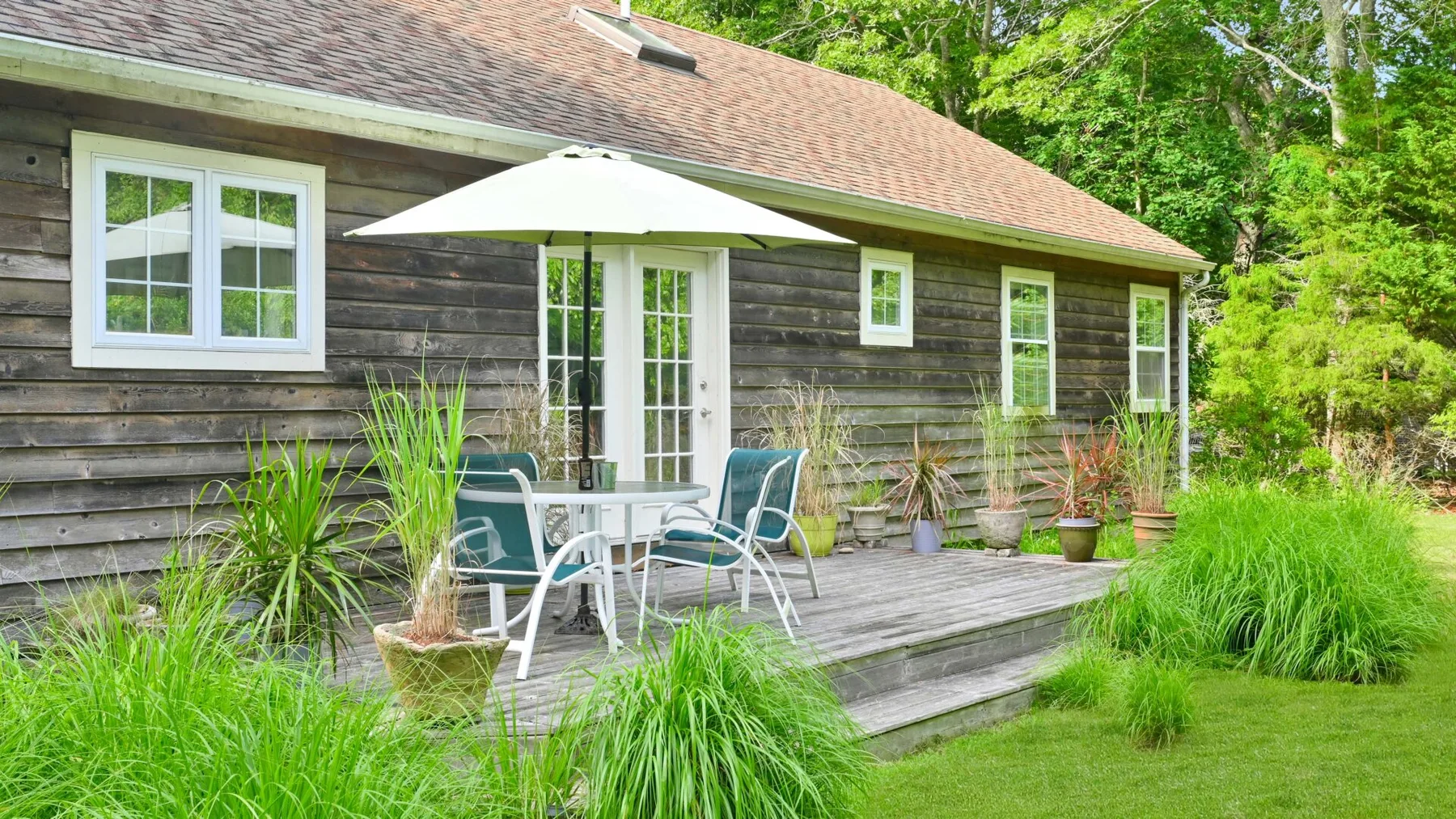 A wooden house exterior with a patio table and umbrella amid greenery.