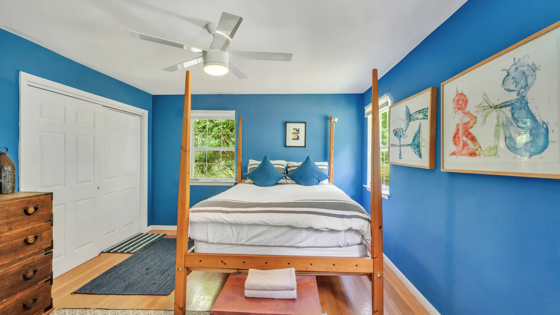 A bedroom with a wooden canopy bed, blue walls, and framed artwork.