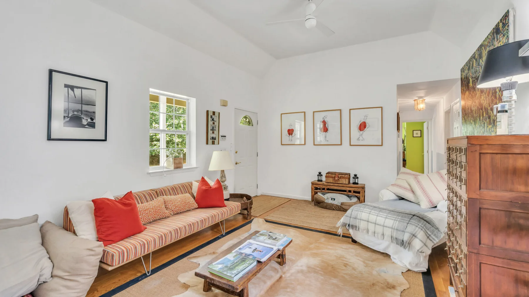 A bright living room with a striped sofa, a bed, and framed artwork.