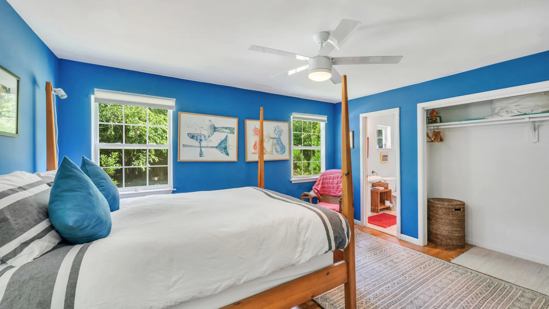 A blue bedroom with a bed, windows, and an open closet.
