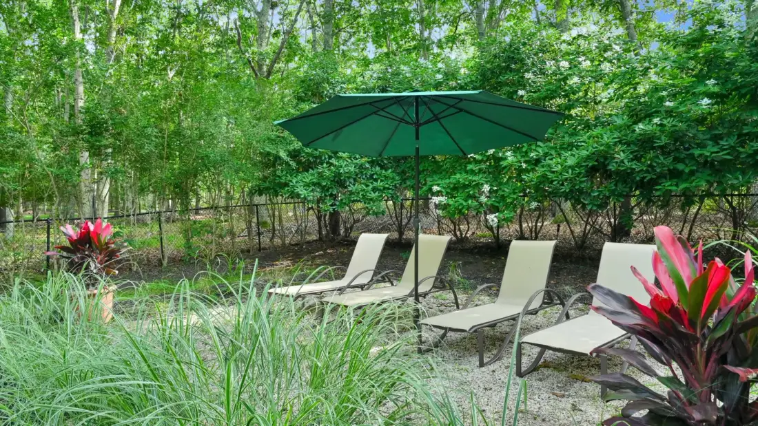 An outdoor garden seating area has lounge chairs beneath a large green umbrella.