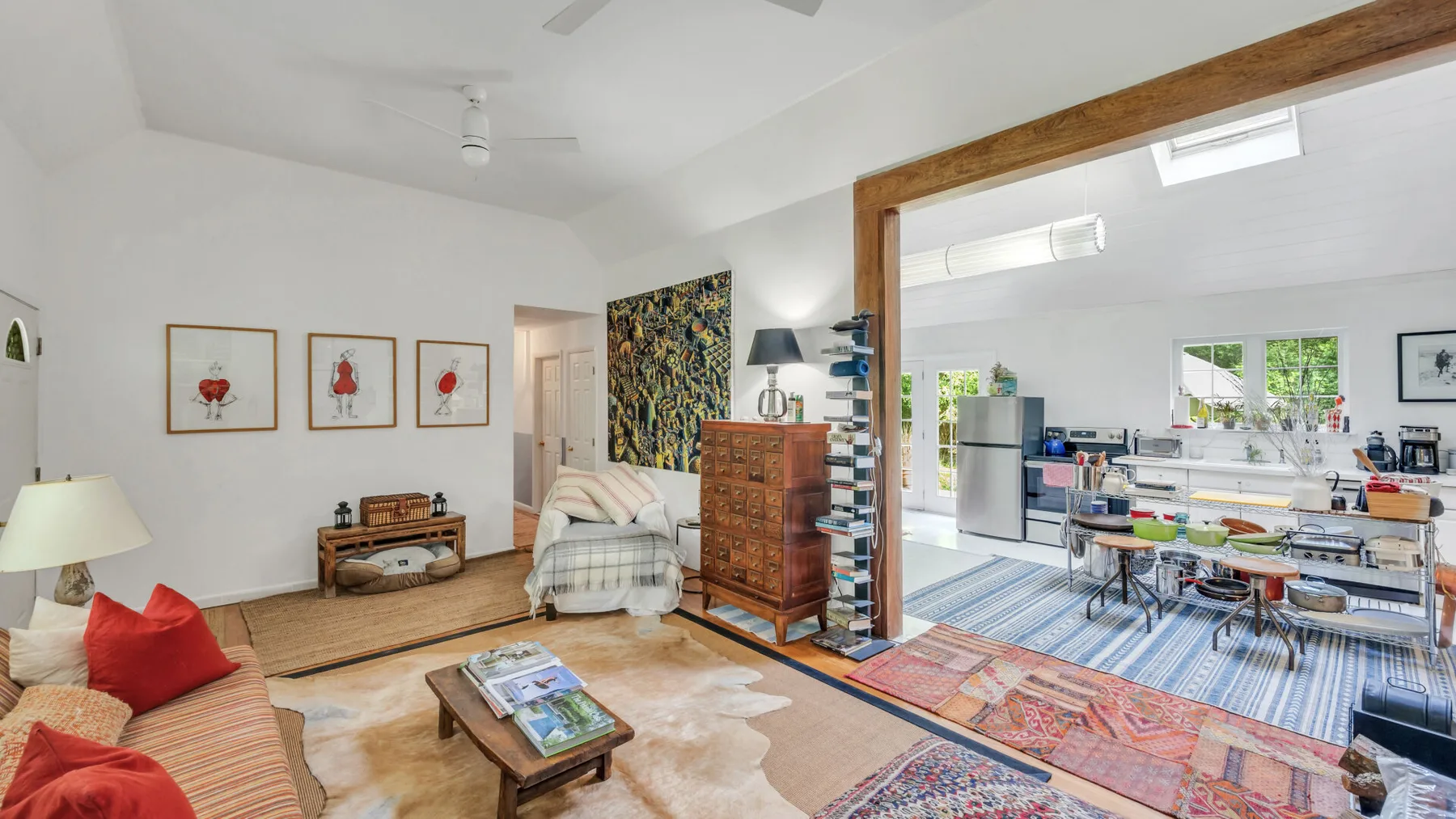 A bright living room opens onto a dining area and kitchen, with colorful rugs and seating.