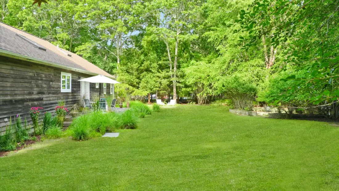 A grassy yard beside a house, with flower beds and leafy trees.