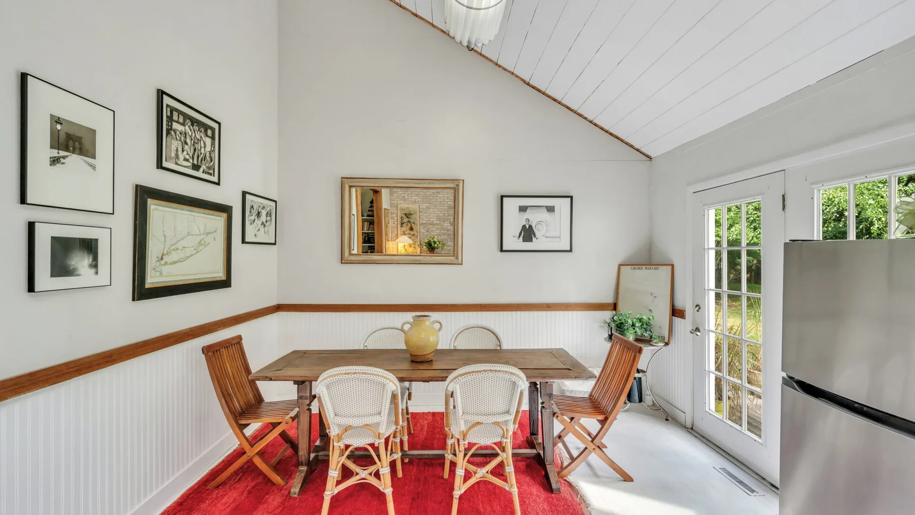 A dining area with a wooden table and chairs beneath framed pictures.