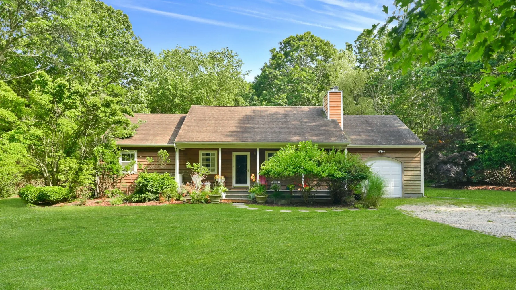 Una casa de una planta se encuentra detrás de un amplio césped verde, rodeada de árboles.