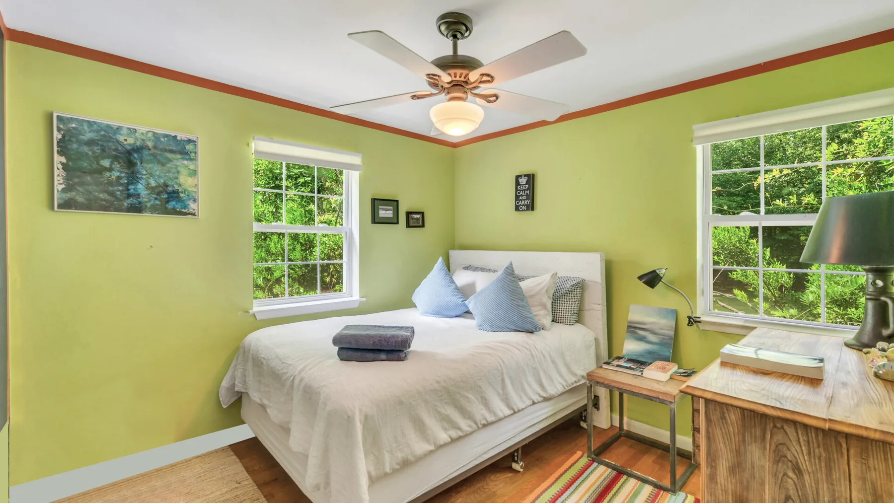 A bedroom with a neatly made bed, two windows, and a ceiling fan.