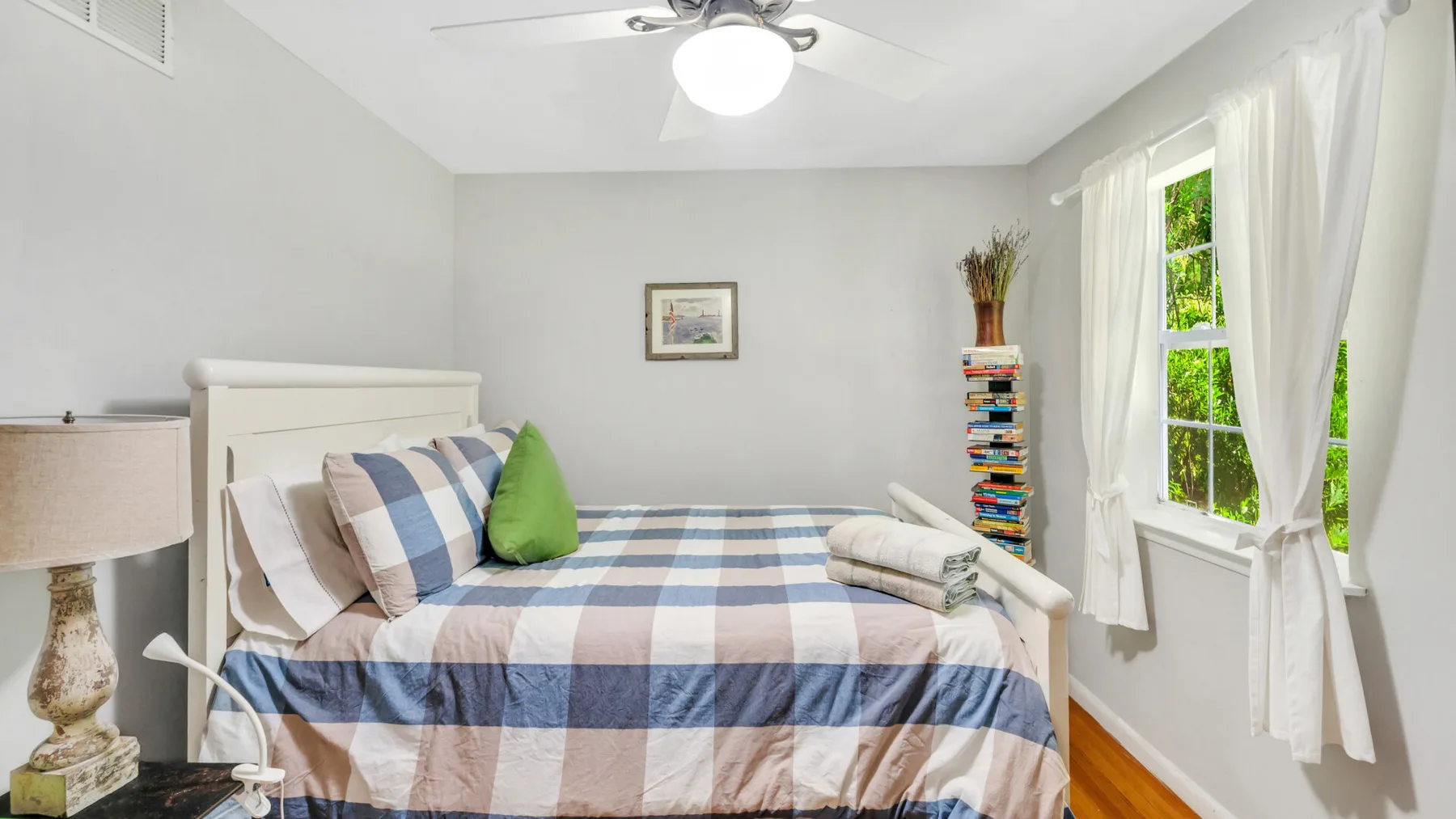 A bedroom with a plaid bed, colorful pillows, and a sunlit window.