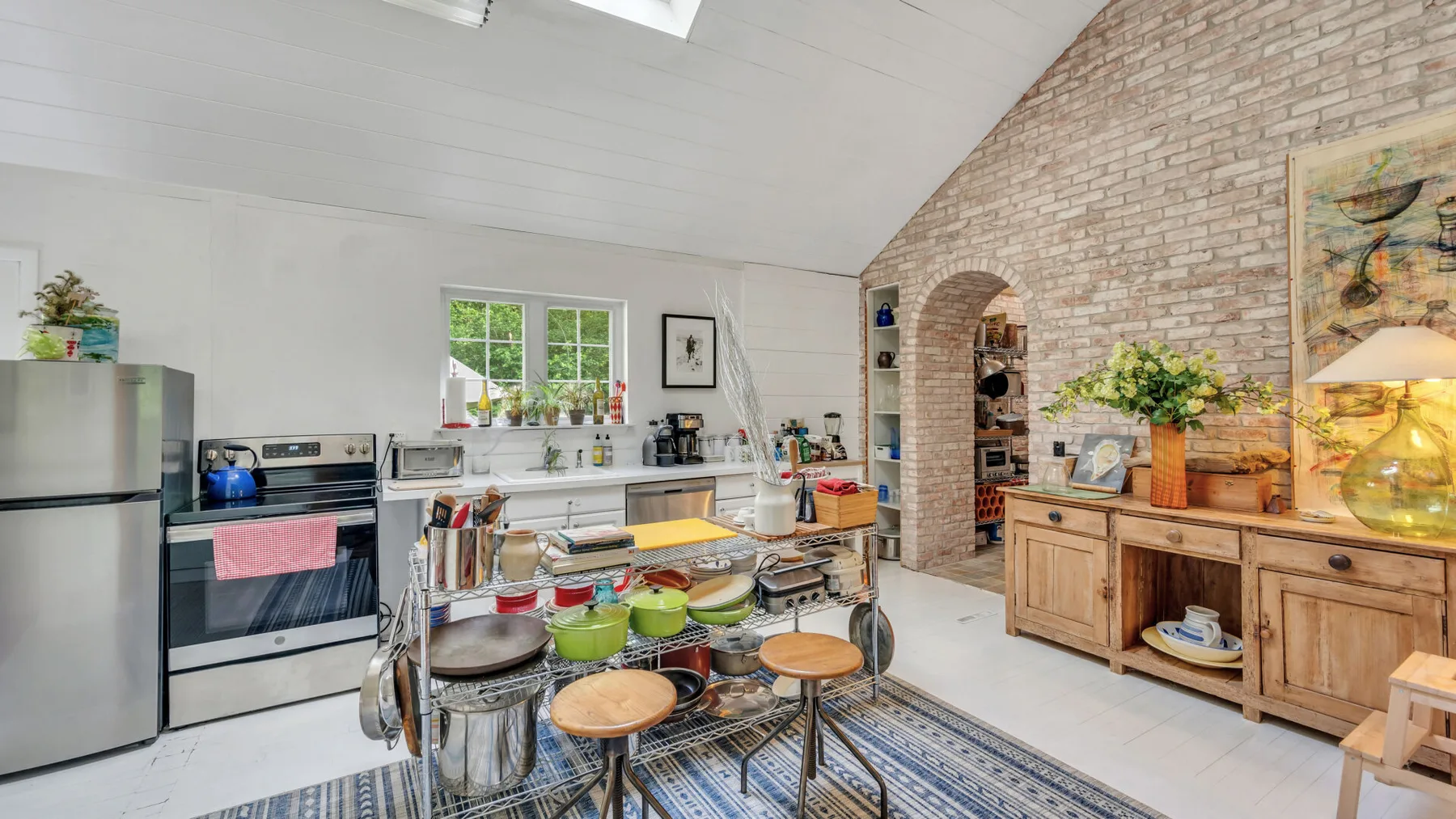 A bright kitchen with a central work island and a brick wall.