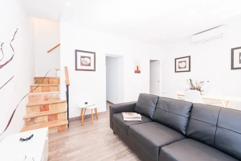 A bright living room with dark seating beside a staircase and framed wall art.