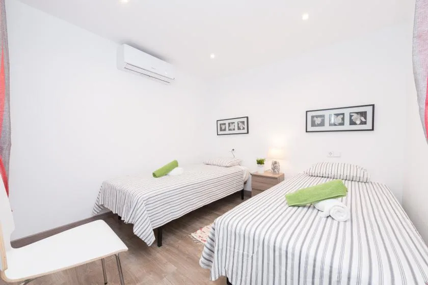 A bright bedroom with two striped beds and a small table between them.