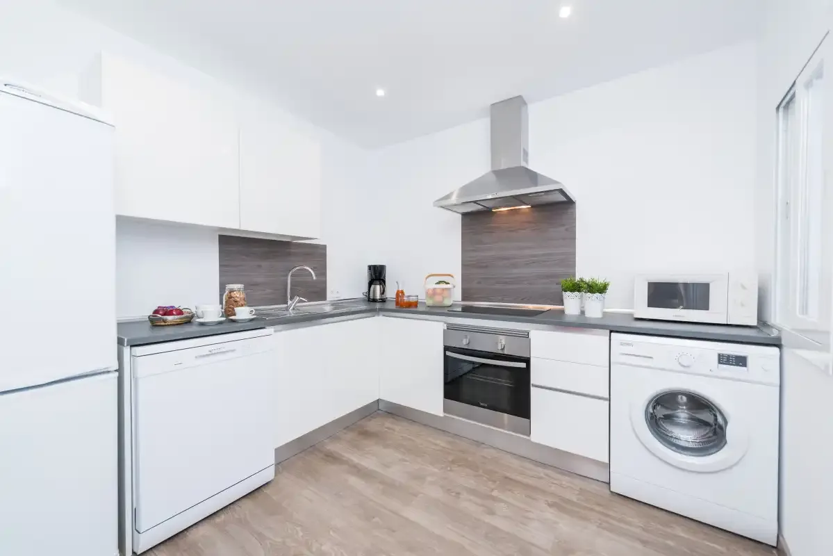 A bright modern kitchen with white cabinets, a cooktop, and a washing machine.