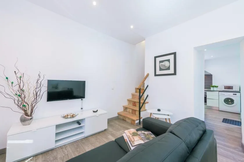 A bright living room with a television, low cabinet, and seating beside a staircase.